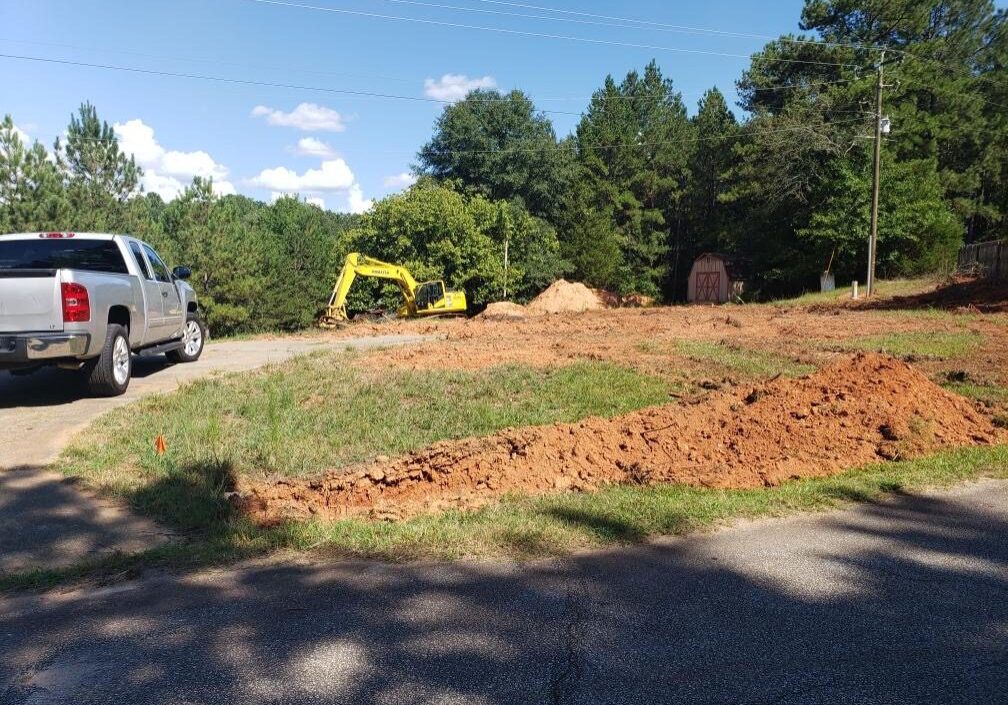 Silver pickup truck on a road going to a site with a yellow excavator vehicle